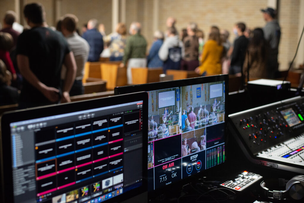 two screens in the production center with people in pews in the background